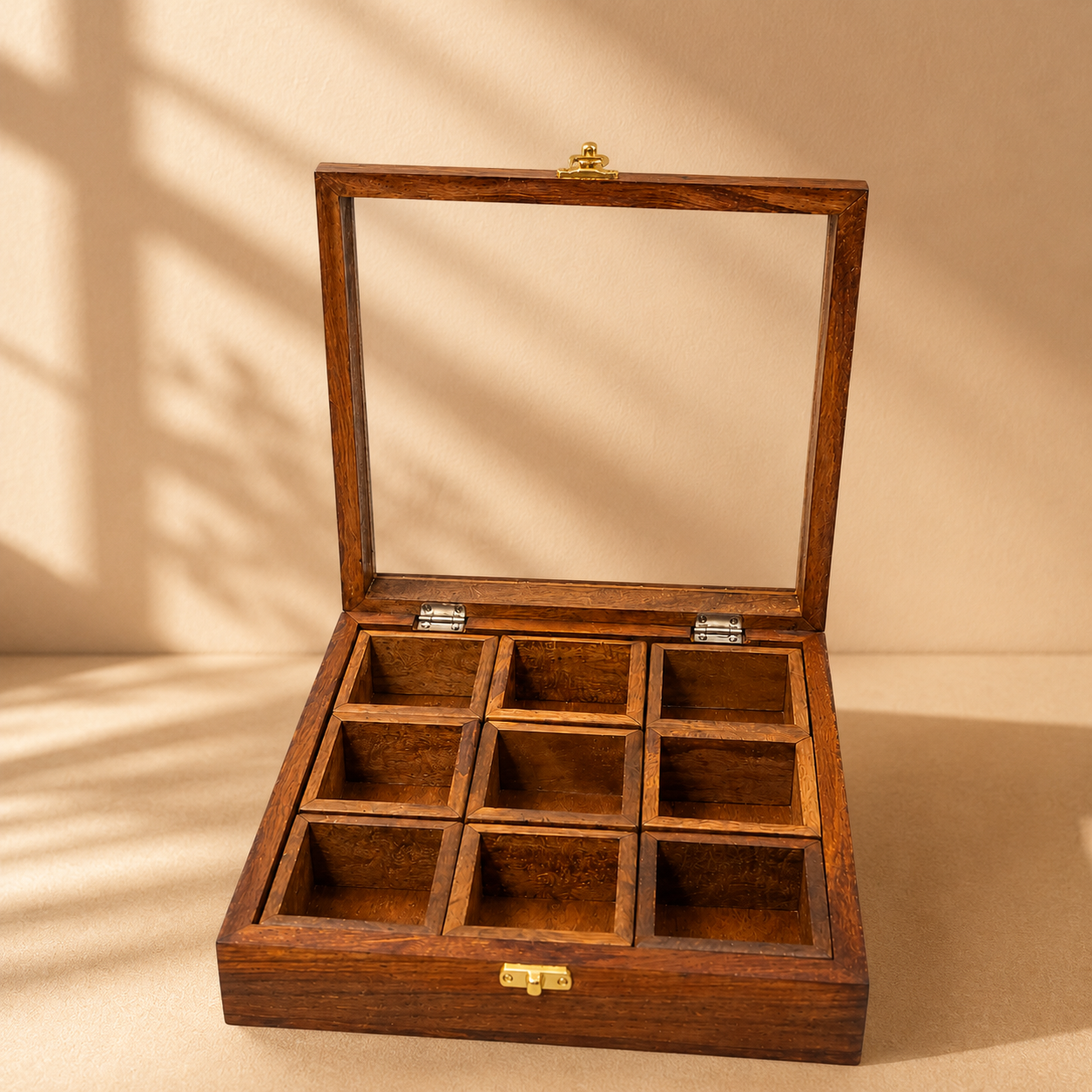 An open wooden display box with a glass lid and nine individual compartments, shown on a warm beige background with soft shadow patterns.