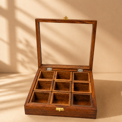 An open wooden display box with a glass lid and nine individual compartments, shown on a warm beige background with soft shadow patterns.